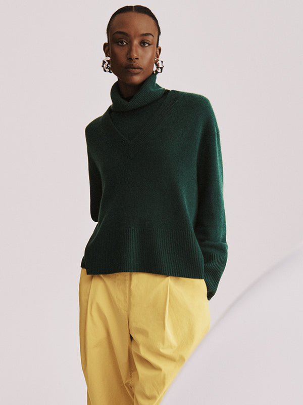 A model wears a White + Warren cashmere sweater in a green jewel tone with gold-tone pants.